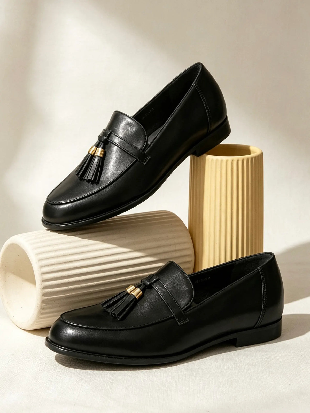 Mocassini neri da donna con nappe esposti in modo elegante su vasi decorativi scanalati in ceramica - SUNTIMEMODA