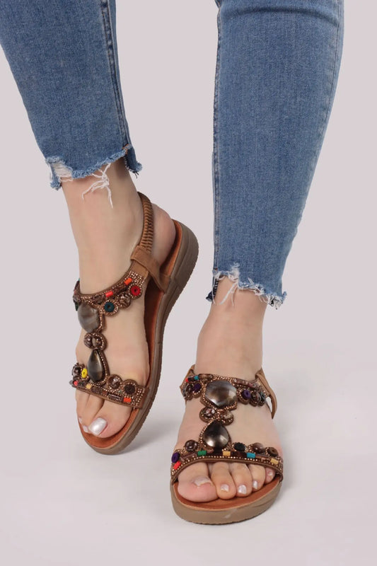 Donna che indossa sandali marroni stile etnico decorati con pietre colorate e strass, abbinati a jeans - SUNTIMEMODA