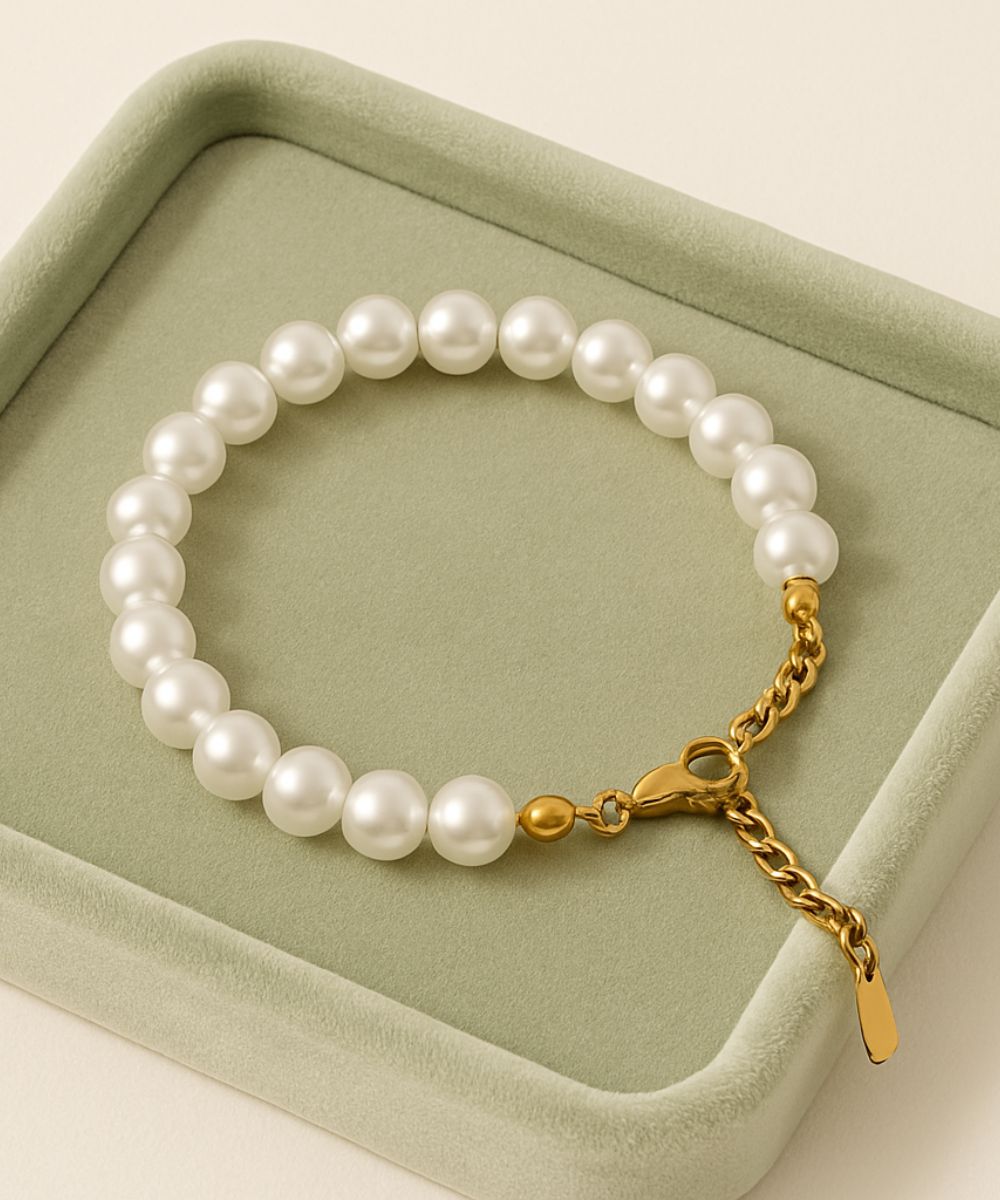 Bracciale di perle bianche luminose adagiato su espositore in velluto verde, dettaglio della finitura oro - Suntime Moda