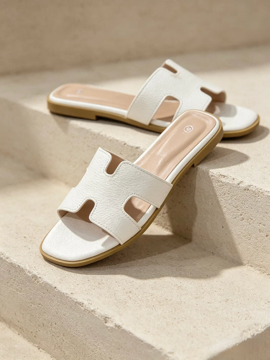 Ciabatte slide da donna bianche con fascia ad H in ecopelle effetto martellato, posate su gradini in pietra chiara - SUNTIMEMODA