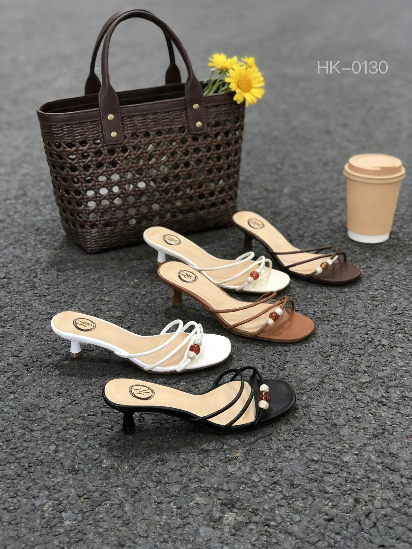Collezione di sabot a fascia unica con tacco gatto basso in 4 colori (bianco, nero, cuoio, caffè scuro) con perline, adagiati a terra accanto a una borsa di paglia intrecciata - SUNTIME MODA