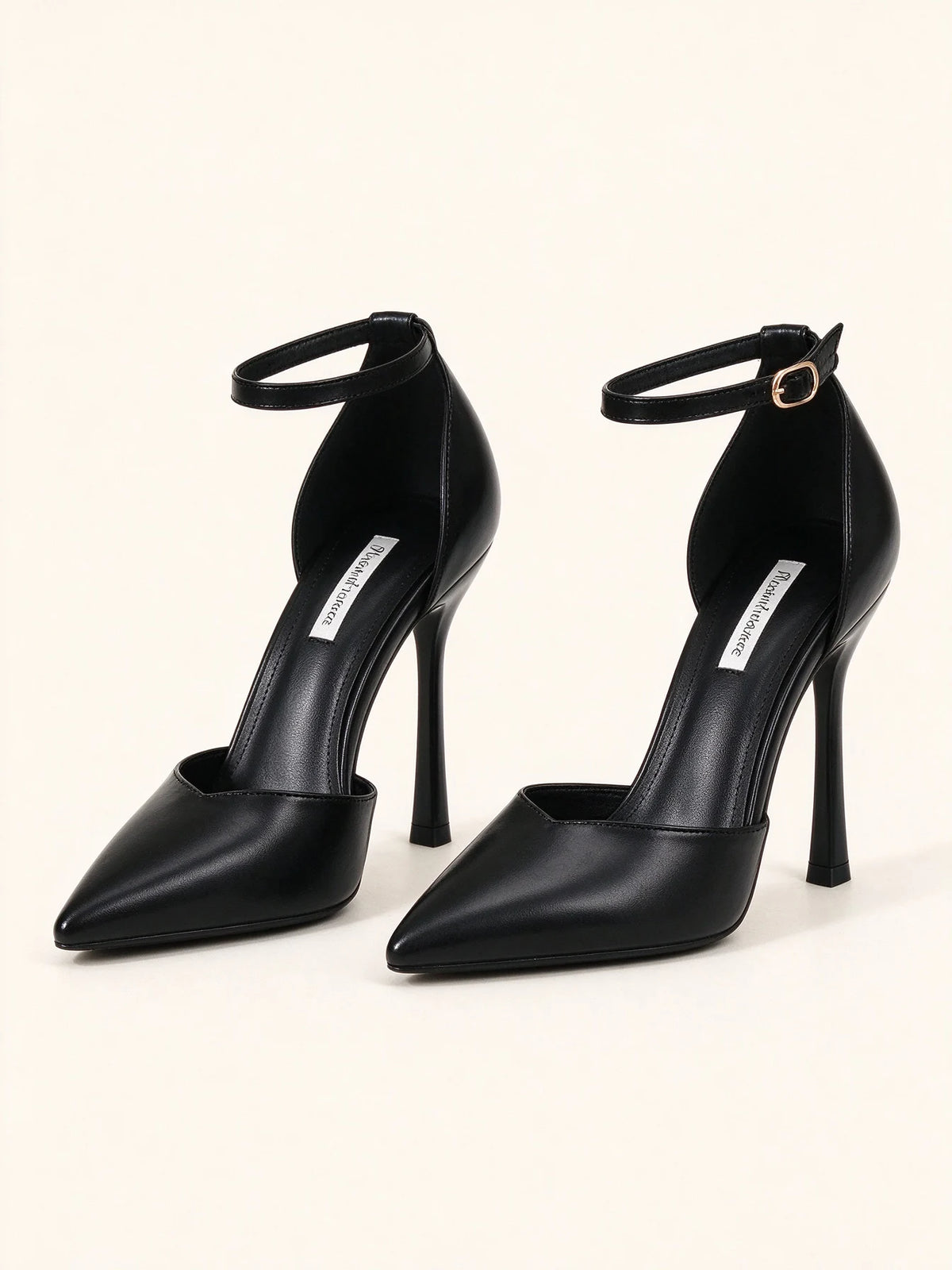 Un paio di eleganti scarpe décolleté nere a punta in ecopelle con cinturino alla caviglia e tacco a spillo alto, su sfondo bianco - SUNTIMEMODA