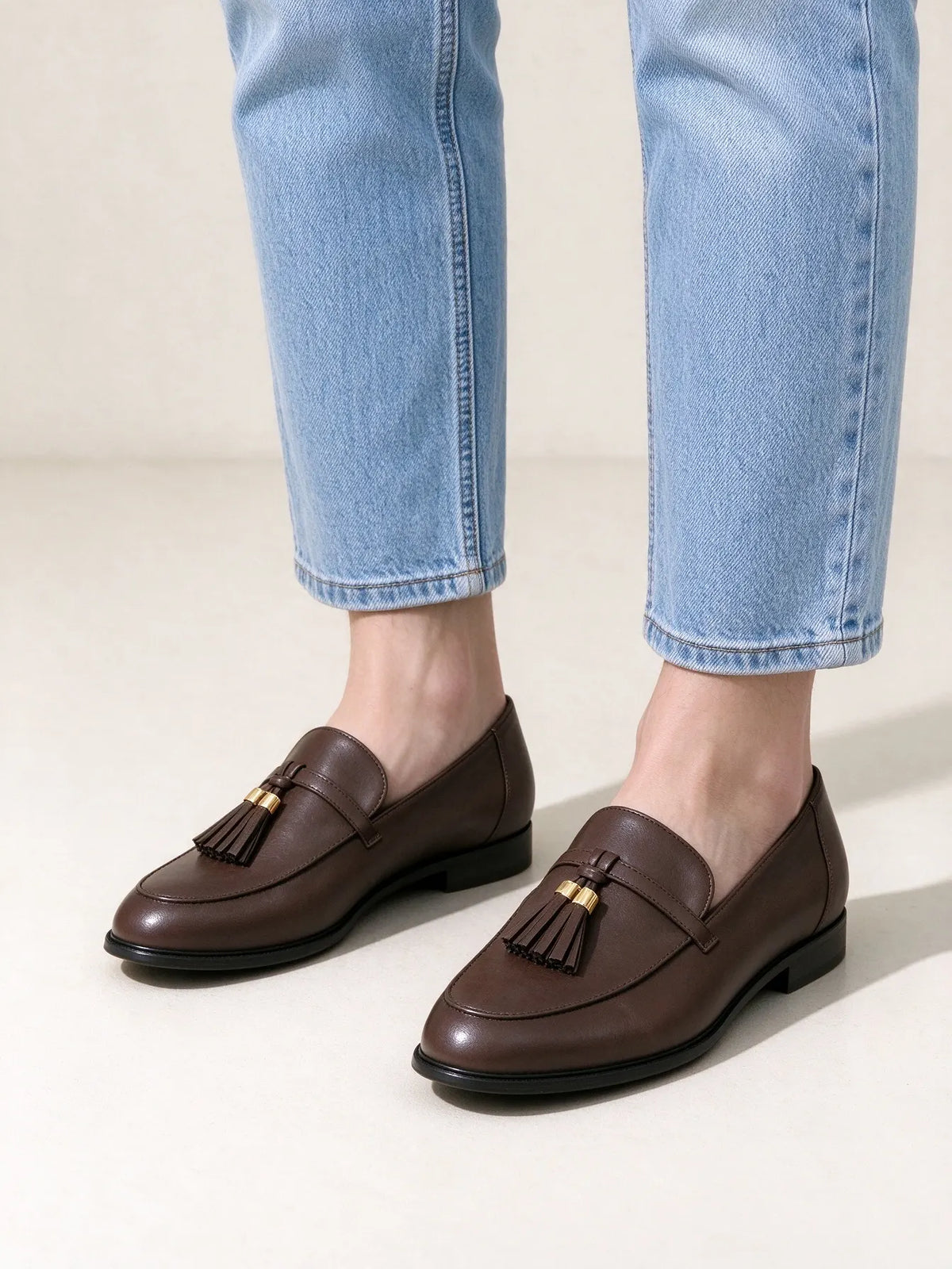 Modella che indossa mocassini marroni con nappe e dettagli dorati, abbinati a jeans chiari per un look casual elegante - SUNTIMEMODA