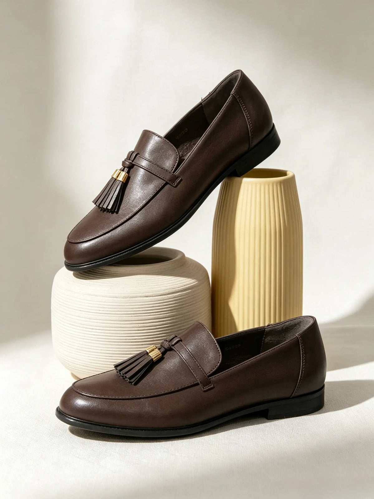 Mocassini marroni da donna con nappe esposti artisticamente su vasi di ceramica strutturati - SUNTIMEMODA