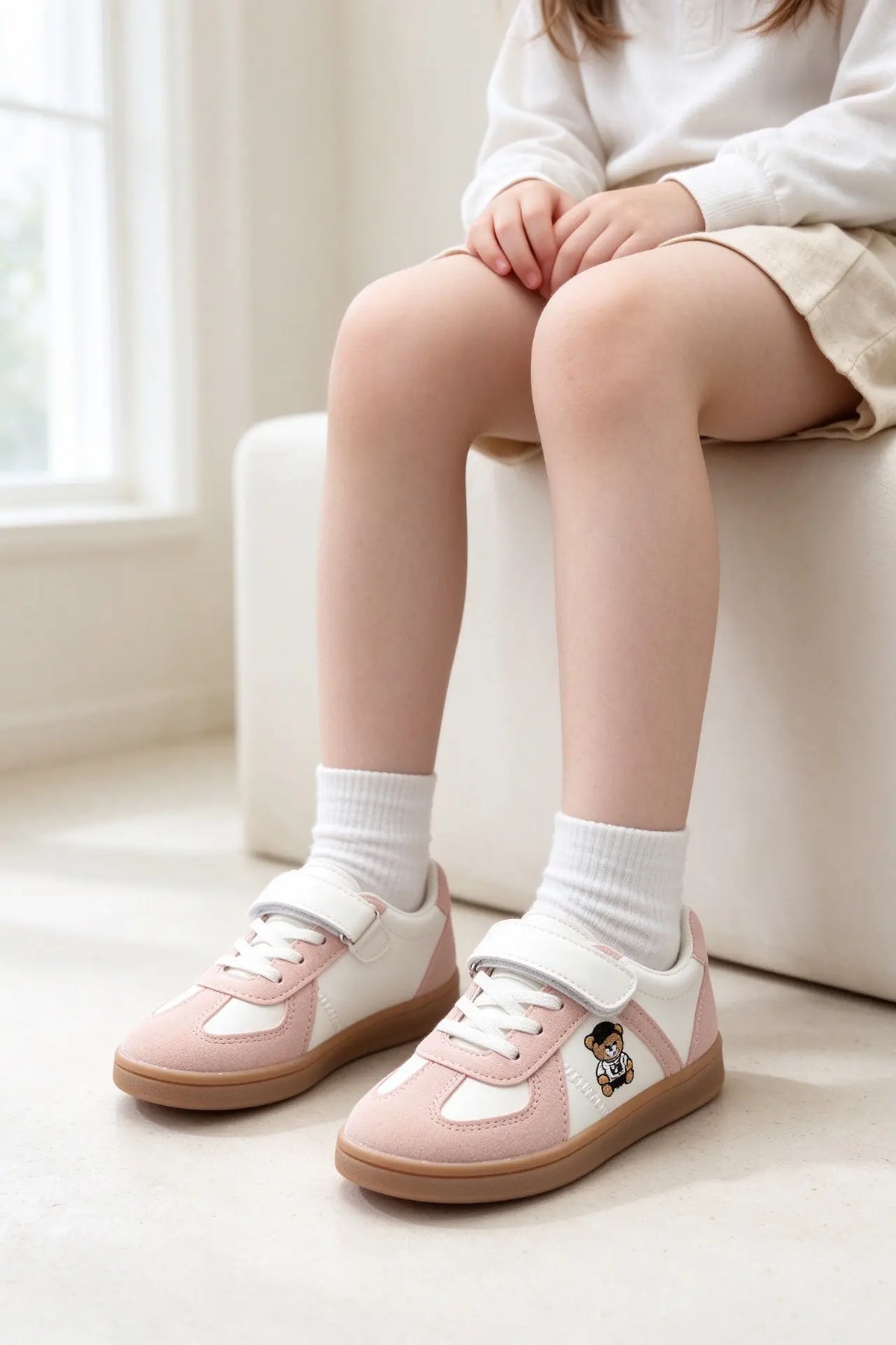 Bambina seduta che indossa adorabili sneakers casual bianche e rosa con chiusura a strappo e un simpatico orsetto ricamato sul lato. - SUNTIMEMODA