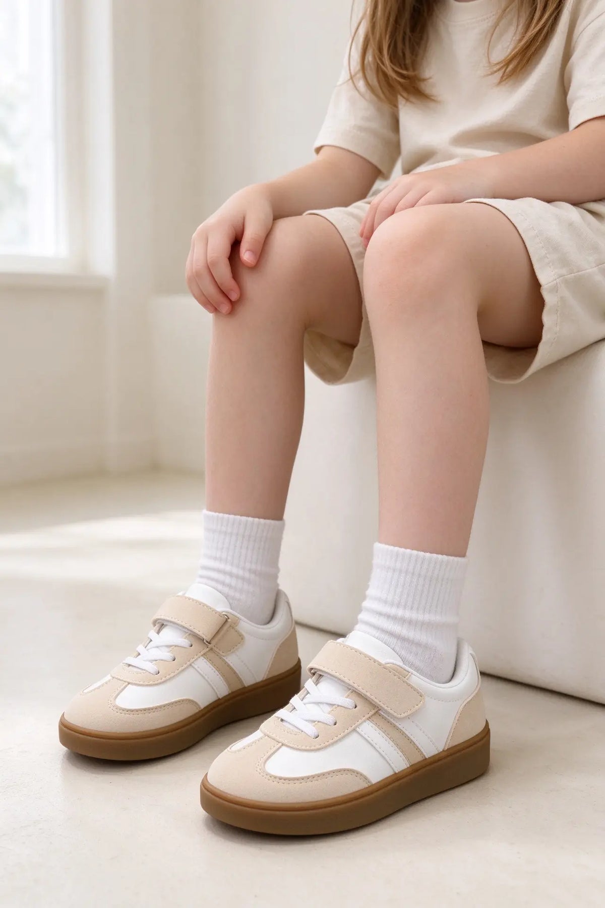 Bambino seduto che indossa un paio di sneakers casual retrò bianche e beige con chiusura a strappo e calzini bianchi, perfette per un look quotidiano - SUNTIMEMODA